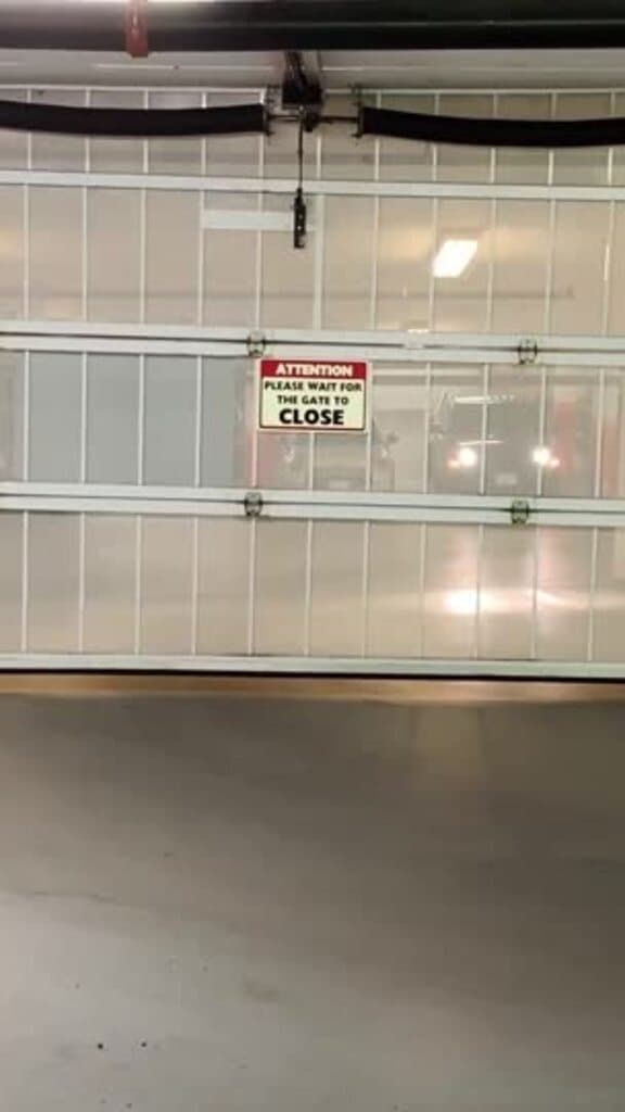 Ceiling-mounted gate operator and control box above an open parkade gate, with a vehicle waiting behind the slatted panel
