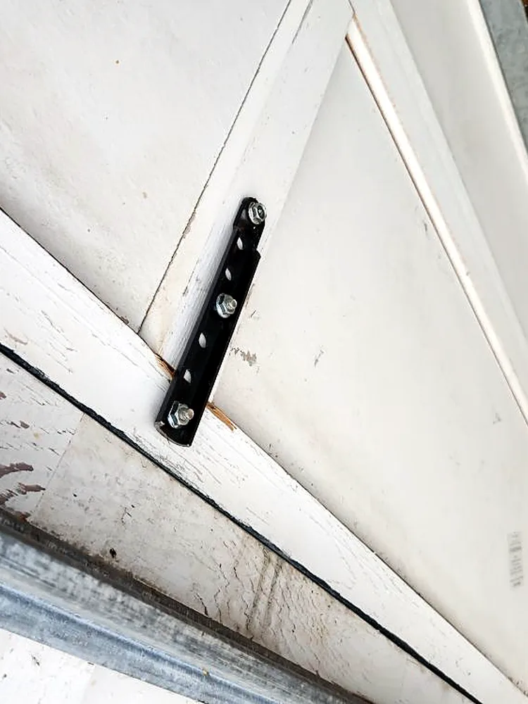 Slotted steel plate bolted across a panel joint on an older painted wood garage door